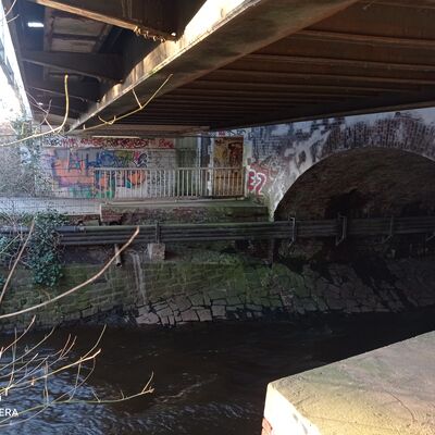 Die Eisenbahnüberführung Mühlenau von Südwesten betrachtet. Im Vordergrund ein Gewässer unter dem Bauwerk.