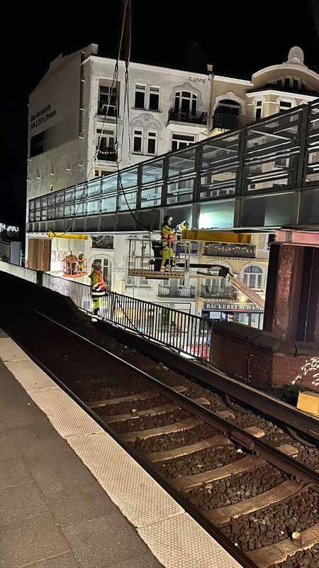 Ein Arbeiter auf einer mobilen Arbeitsbühne führt Arbeiten an einer Kabelhilfsbrücke durch, im Vordergrund ein weiterer Arbeiter neben einem Bahngleis