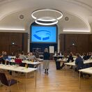 Die Mitglieder des Brückenforums sitzen in einem Sitzungssaal vor einer Präsentation auf einer Leinwand.